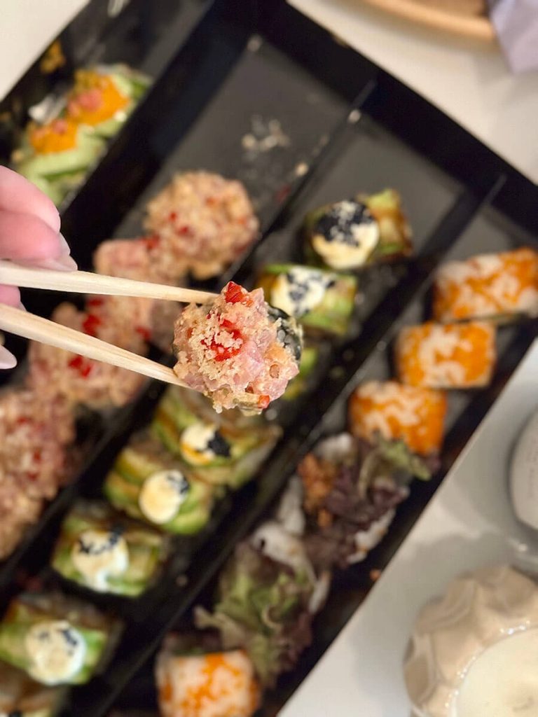 woman eating sushi roll out of a box with many selections