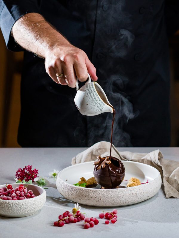 Chef pouring hot chocolate over desert