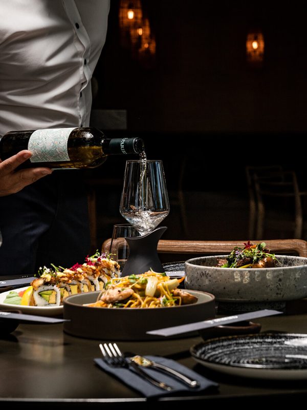 Waiter serving wine at a table with asian dishes
